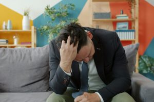 man-in-suit-sitting-on-couch-with-head-in-hands